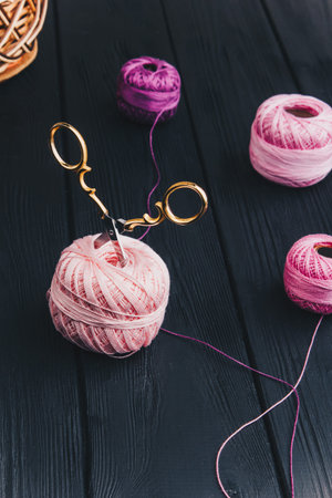 Golden steel scissors on black boards are stuck into a pink silk skein of knitting thread.