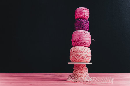A collection of knitting skeins stacked on top of each other on a pastel pink wooden surface with a black background behind.の写真素材