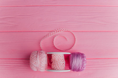 Colorful yarn and sewing tools lie neatly on a bright pink wooden surface, creating a fun craft...