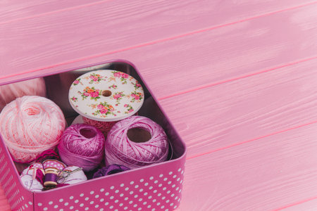 Craft supplies in a polka-dot tin box with pink and purple yarn, ribbon, and sewing accessories on a...