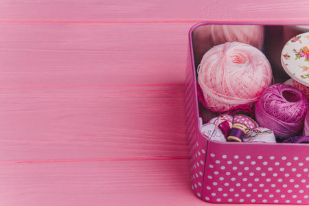 Craft supplies in a polka-dot tin box with pink and purple yarn, ribbon, and sewing accessories on a...