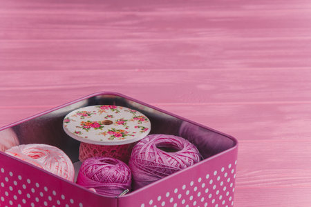 A tin box filled with colorful balls of yarn and sewing supplies on a pink wooden surface. Perfect for crafting.の写真素材