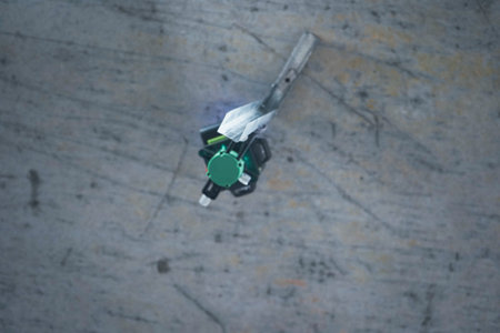 A compact green laser level sits on a tripod set up in an unfinished room with exposed brick walls.の写真素材