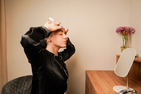 Woman in black pajamas and with a headband doing beauty procedures at home. Girl doing facial massage with her hands. Applying cream to face.の写真素材