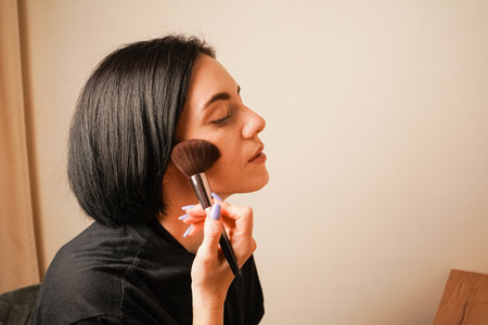 With a steady hand, a woman uses a brush to apply makeup to her face. Her smooth skin and natural elegance take center stage. The scene reflects a peaceful, intimate moment.の写真素材