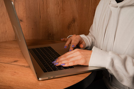 Hands are seen typing on a laptop keyboard placed on a wooden table. The close-up shot emphasizes...
