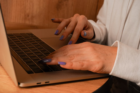 Hands are seen typing on a laptop keyboard placed on a wooden table. The close-up shot emphasizes...
