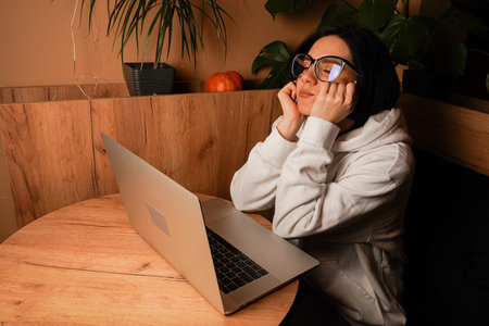 Resting her chin on her hands, a woman gazes thoughtfully at her workspace. The warm lighting and...