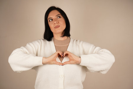 Smiling gently, the woman makes a heart gesture with her hands, symbolizing care and connection. Her relaxed posture conveys calm and sincerity. The gesture forms a heart in front of the eyes.の写真素材