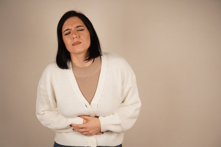 Her facial expression and posture convey a clear sense of unease. This gesture emphasizes physical tension. The girl is holding her hands on her stomach, seemingly in discomfort or pain.の写真素材