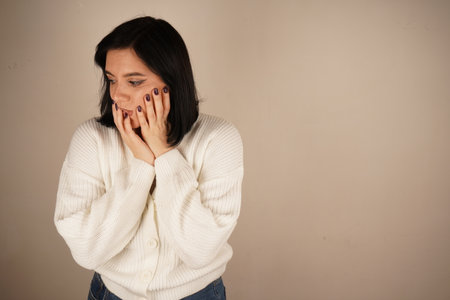 A young woman holds her hands over her face, her eyes wide open and her mouth open in genuine surprise. The interesting facial expression conveys a moment of surprise. The focus is on her emotions.の写真素材