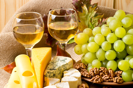 White wine with blue cheese, camembert and swiss cheese, walnuts and grapes on sackcloth on a background of a wooden wall and autumn leavesの写真素材