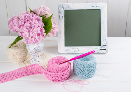 Yarn for crochet and handmade on white wooden boards in shabby chic style and photo frame with hortensia in vaseの写真素材