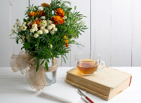 Old book and wooden nib pen with sheet paper and tagetes bouquet on wooden board in shabby chic styleの写真素材