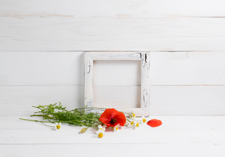 Daisy flowers with red poppies bouquet and photo frame on white wooden shabby board. Home interior.の写真素材