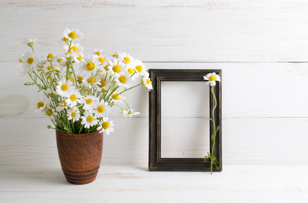Daisy flowers bouquet with photo frame on white wooden shabby board. Home interior.    の写真素材
