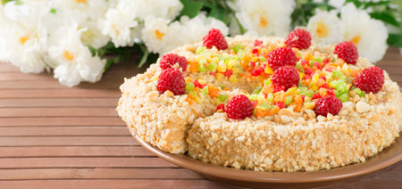 Cake with nuts, candied fruits and raspberries on  bamboo mat and flowers