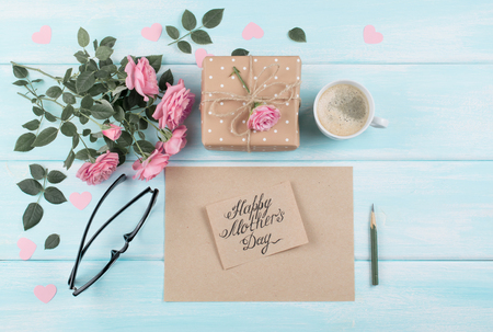 Pink roses with paper greeting card, gift box and coffee cup for Mothers day on background of shabby wooden planks. Top view. Flat design.の写真素材