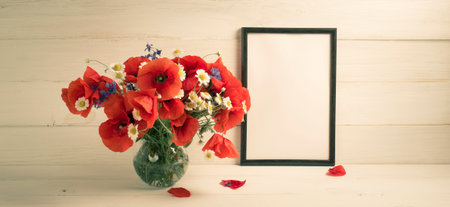 Red poppies bouquet in round vase and motivational frame for text on background of white wooden...