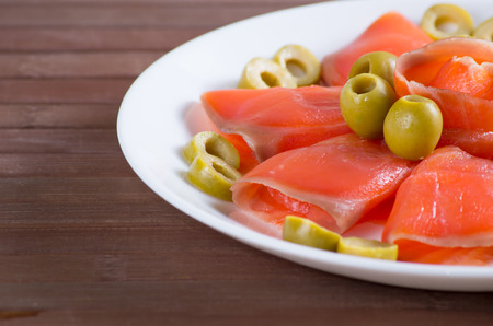 Sliced salted salmon served with olive on white plateの写真素材