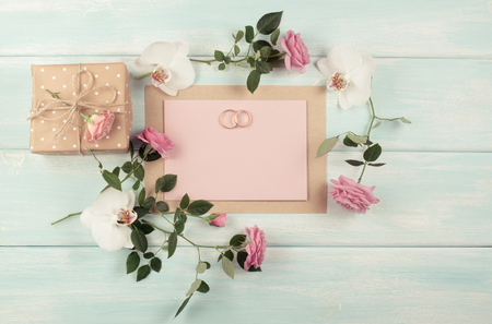 Pink roses, orchid, bridal rings and gift box with emty paper for wedding invitations on background of shabby wooden planks. Top view. Flat design. Copy space.の写真素材