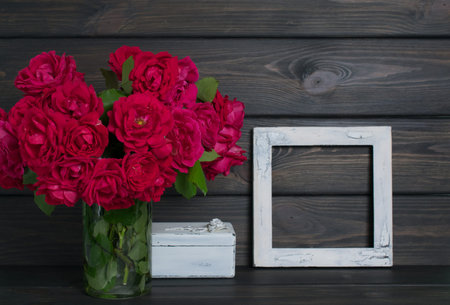 Roses in vase and and vintage photo frame on background of wooden planks in rustic style....
