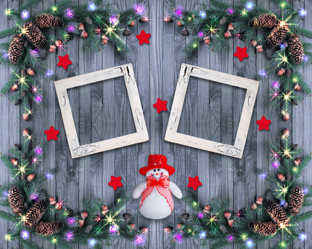 Christmas background with photo frame, snowman and glowing garland with illumination, spruce branches, pine cones and acorns. New Year winter composition.の写真素材