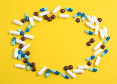 Medical theme. Pharmaceutical colorful pills and capsules on yellow background. Empty place for...