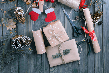 Christmas background. Packed gifts and scrolls, spruce branches and tools on shabby wooden table. Workplace for preparing handmade new year decorations. Winter holidays concept. Top view.の写真素材