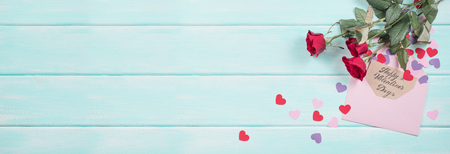 Red roses with paper hearts and greeting card with hand drawn inscription for Valentine day with place for text on background of shabby wooden planks. Top view and flat design.の写真素材