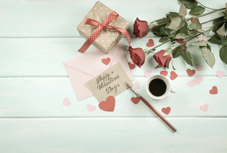 Valentine day theme. Top view of roses, hearts, packed gifts, coffee cup and envelope on shabby wooden table. の写真素材