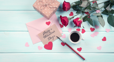 Valentine day theme. Top view of roses, hearts, packed gifts, coffee cup and envelope on shabby wooden table. の写真素材