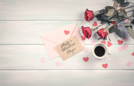 Valentine day theme. Top view of roses, hearts, coffee cup and envelope on shabby wooden table. の写真素材