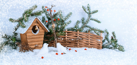 Christmas winter background with birdhouse and two birds pecking red berries on snow. New Year handmade home decor.の写真素材