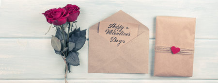 Valentine day theme. Top view of roses bouquet and eco paper with text. Packed gifts and envelope on...