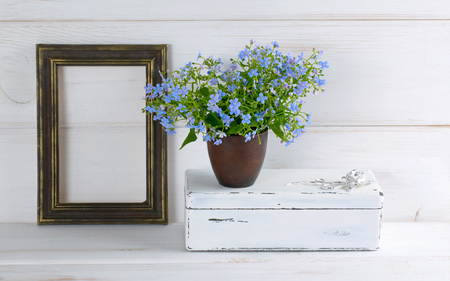 Forget-me-not flowers bouquet in clay cup, vintage casket and photo frame on white wooden shabby board in provence styleの写真素材