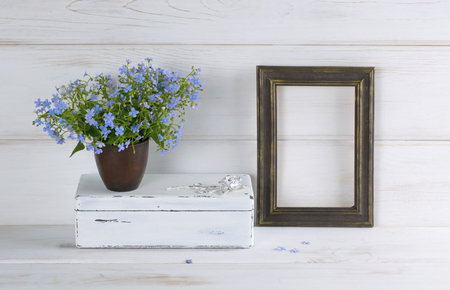 Forget-me-not flowers bouquet in clay cup, vintage casket and photo frame on white wooden shabby board in provence styleの写真素材