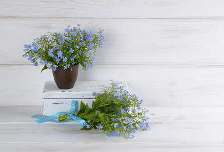 Forget-me-not flowers bouquet in clay cup and vintage casket on white wooden shabby board in provence styleの写真素材