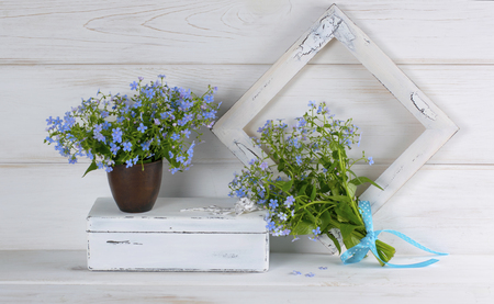 Forget-me-not flowers bouquet in clay cup, vintage casket and photo frame on white wooden shabby board in provence styleの写真素材