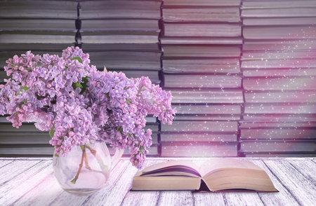 Room interior with lilac flowers in glass vase and open fairytale book on table in shabby chic style on background of stack of old booksの写真素材