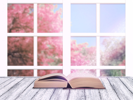 Room interior with open book on table in shabby chic style and sakura blossom outside the windowの写真素材