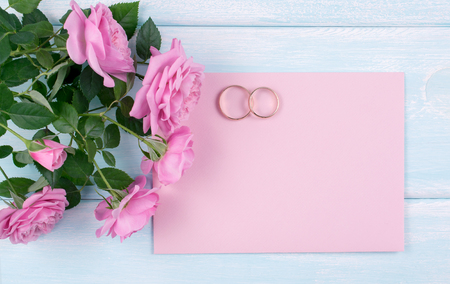 Top view of pink roses and bridal rings with paper greeting card for wedding on background of shabby wooden planks and place for your textの写真素材