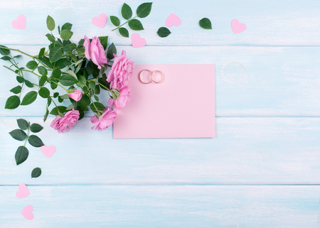 Top view of pink roses and bridal rings with paper greeting card for wedding on background of shabby wooden planks and place for your textの写真素材