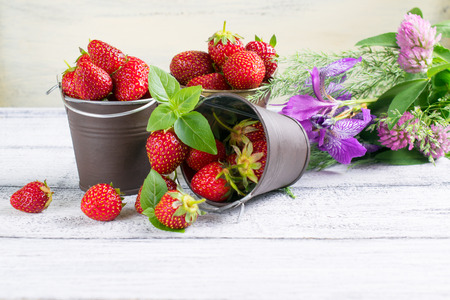 Strawberry in a small bucket and flowers on the wooden boardの写真素材