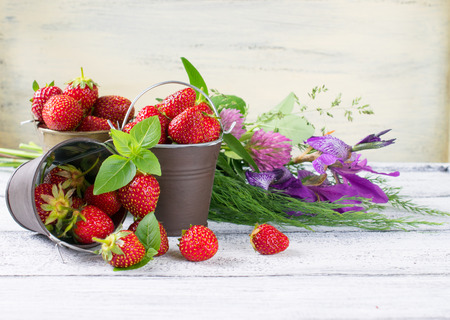 Strawberry in a small bucket and flowers on the wooden boardの写真素材