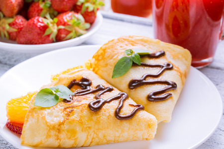 Pancakes with sliced strawberries and chocolate on the shabby wooden boardsの写真素材