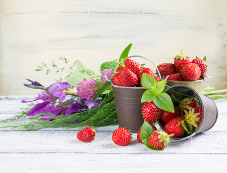 Strawberry in a small bucket and flowers on the wooden boardの写真素材