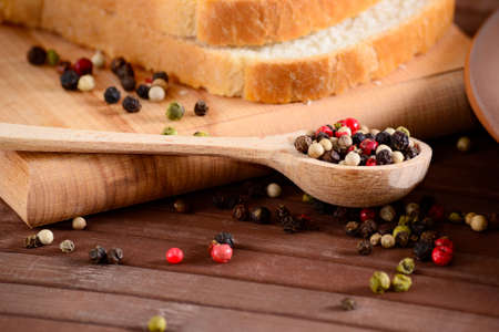 Set of black, pink, white and green pepper corns in wooden spoon on bamboo board and sliced toast bread. Mixed colorful peppercorns spieces.の写真素材