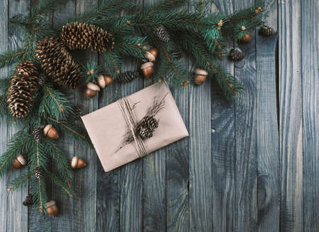 Christmas background with kraft paper gift package in vintage style, spruce fir tree branches with cones and oak acorns on wooden planks in rustic style, New Year winter holidays theme.の写真素材