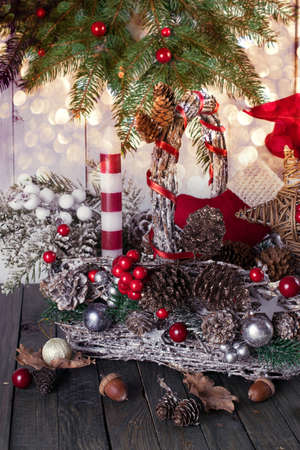 Christmas background with wicker basket, Santa boot and hat, candle and star, fir tree, acorns, pine, spruce cones on table, New Year winter holiday home natural material decor, glowing festive bokeh.の写真素材